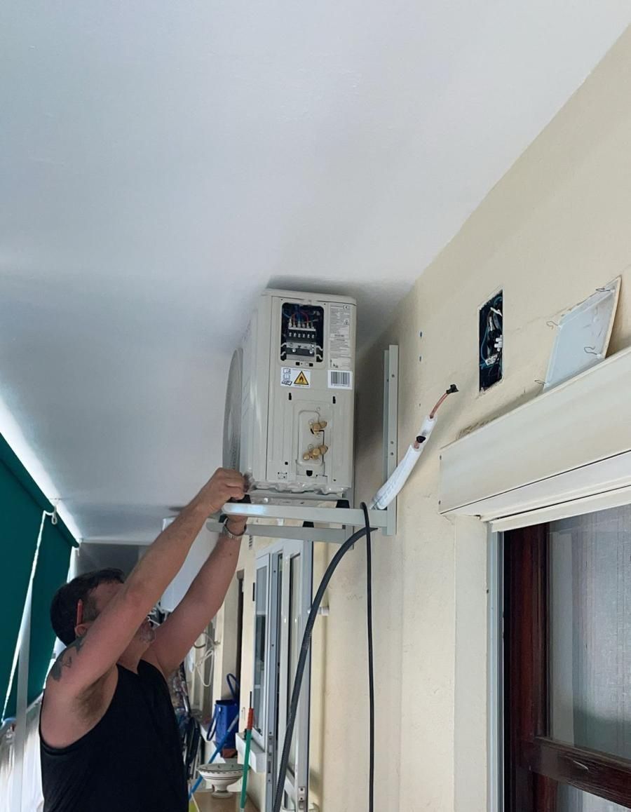 Un hombre está instalando un aire acondicionado en un balcón.